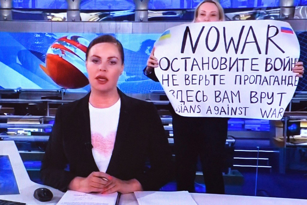 Seorang wanita melihat layar komputer menonton seorang karyawan Rusia Channel One yang membangkang memasuki studio TV Ostankino secara langsung selama siaran berita malam yang paling banyak ditonton di Rusia.