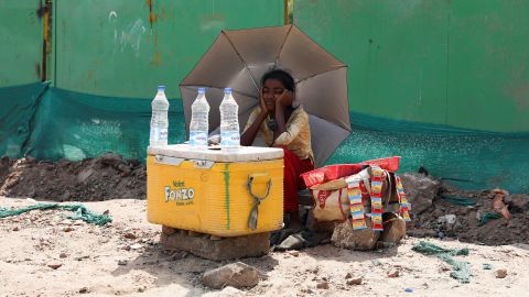 Seorang gadis penjual air menggunakan payung untuk melindungi dirinya dari sinar matahari di New Delhi.