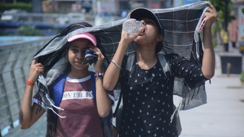 Gadis-gadis menutupi kepala mereka saat mereka berjalan dan minum air di siang hari yang terik di Mumbai.