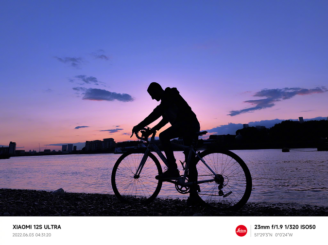 Contoh bidikan yang diambil dengan Xiaomi 12S Ultra, menunjukkan pengendara sepeda di tepi sungai di pagi hari sebelum matahari terbit.