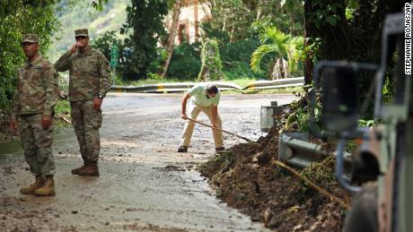 Pasukan Garda Nasional mengarahkan lalu lintas saat Residen Luis Nogueira membantu membersihkan jalan yang rusak akibat Badai Fiona di Cayai, Puerto Rico, Selasa.