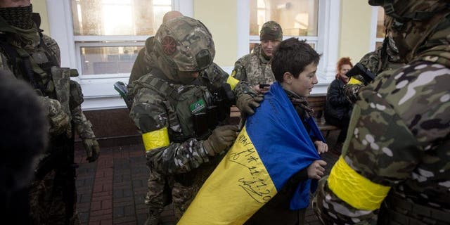 Seorang anak laki-laki memegang bendera nasional Ukraina yang ditandatangani oleh anggota militer Ukraina, 19 November 2022, di Kherson, Ukraina.