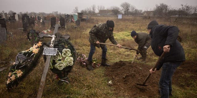 Penduduk dan pejabat Ukraina menggali jenazah seorang gadis berusia 16 tahun dan tujuh pria lainnya yang dibunuh oleh pasukan Rusia dan dimakamkan di kota Pravdin, di pinggiran Kherson, pada 29 November 2022.